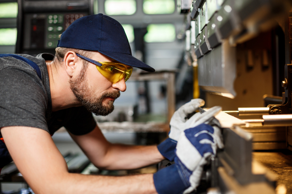 Mann mit Schutzbrille und Schutzhandschuhen schaut prüfend eine Maschine an.